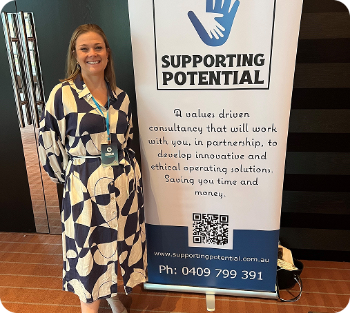 Angela beside a Supporting Potential pull-up banner at a conference